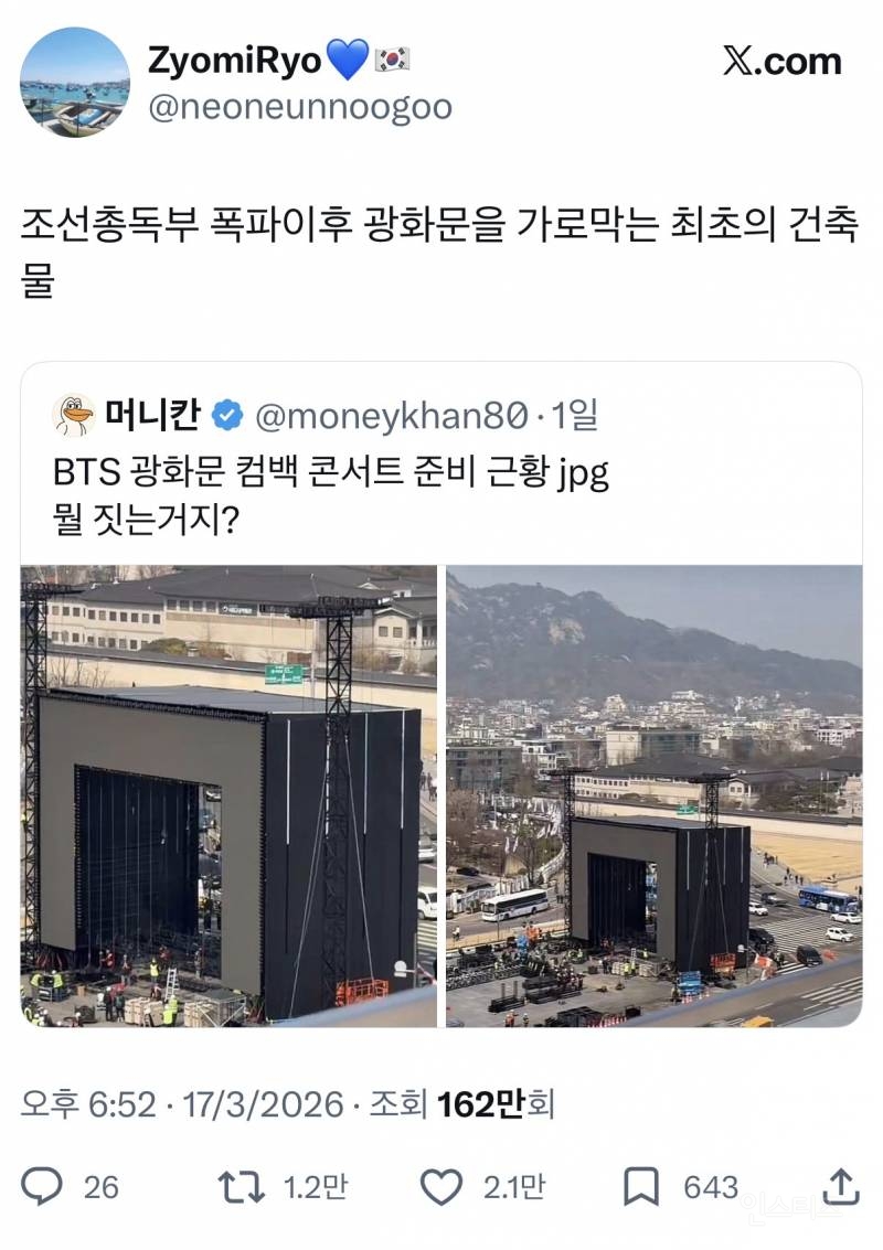 A wide shot of the massive BTS installation standing in front of the historic Gwanghwamun gate in Seoul.