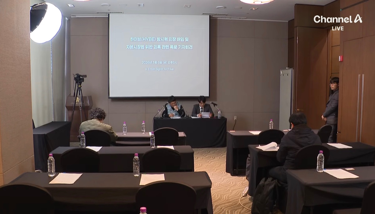 記者会見壇上のマイクと背景のロゴ。複数のメディアが参加していることを示唆するが、実際の参加者数は限定的だったと報じられている。