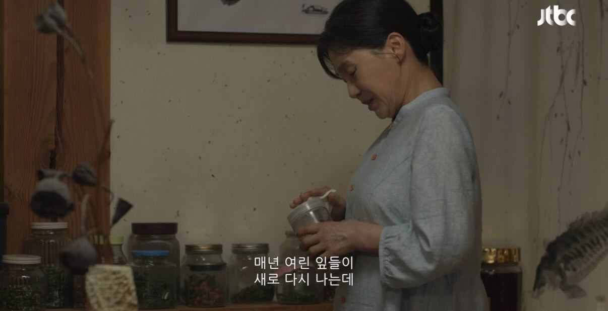 A wide shot of a modern, minimalist interior with large windows looking out onto a city skyline. A lone figure stands by the window, contemplating the view.